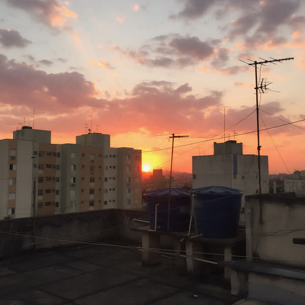 Pôr do sol laranja atrás de prédios e antenas, visto de uma laje.