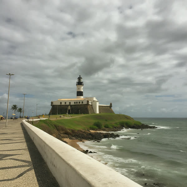 Farol branco sobre um morro verde à beira-mar, com céu nublado.